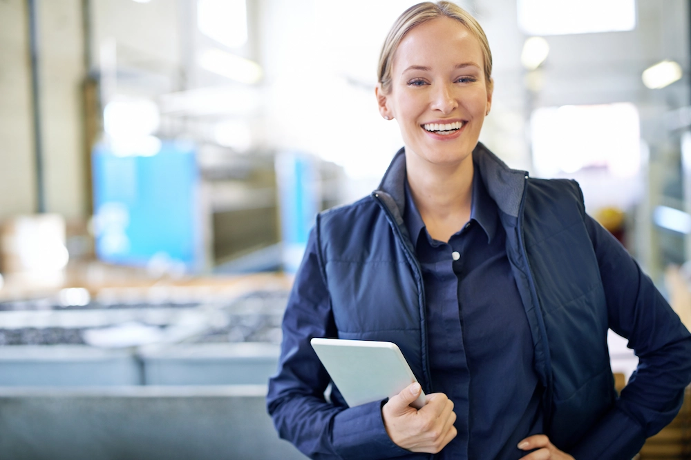Smiling supervisor holding a tablet computer in a manufacturing plant.